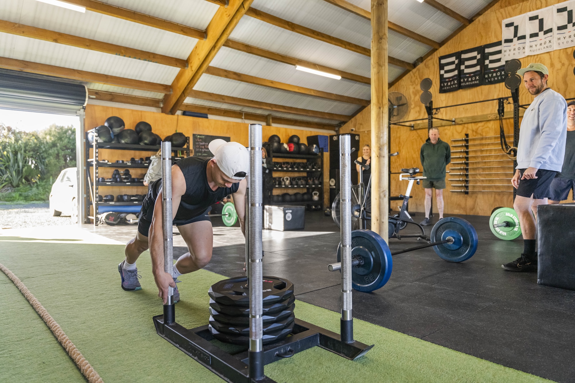 A member pushing a weighted sled across the turf strip in the open gym