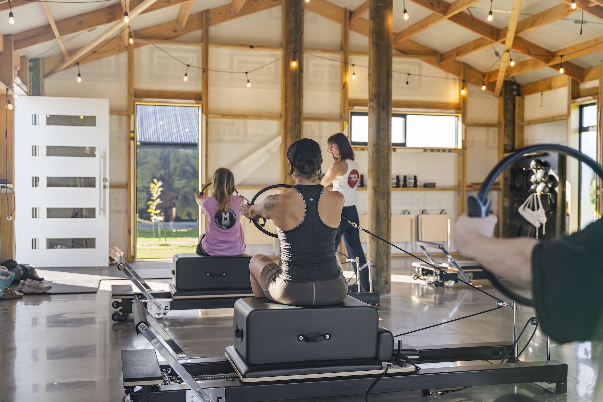 A reformer pilates class working with magic circles under the festoon lights
