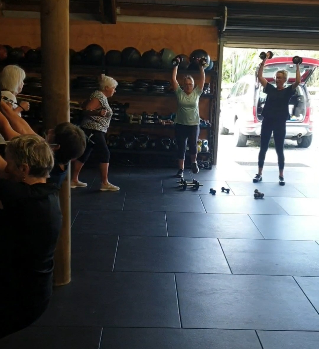 Members of the over-60s class pressing dumbbells overhead in the open gym